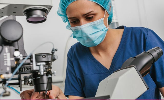 Lab technician analyzing embryos with a microscope for Preimplantation Genetic Testing for Aneuploidy (PGT-A) in an IVF clinic