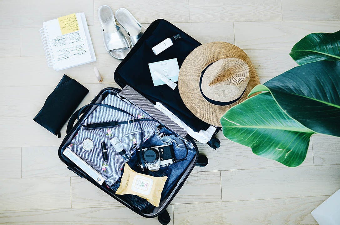 Open suitcase with travel essentials, including a hat, sandals, and toiletries, symbolizing preparation for a vacation while managing fertility treatments.