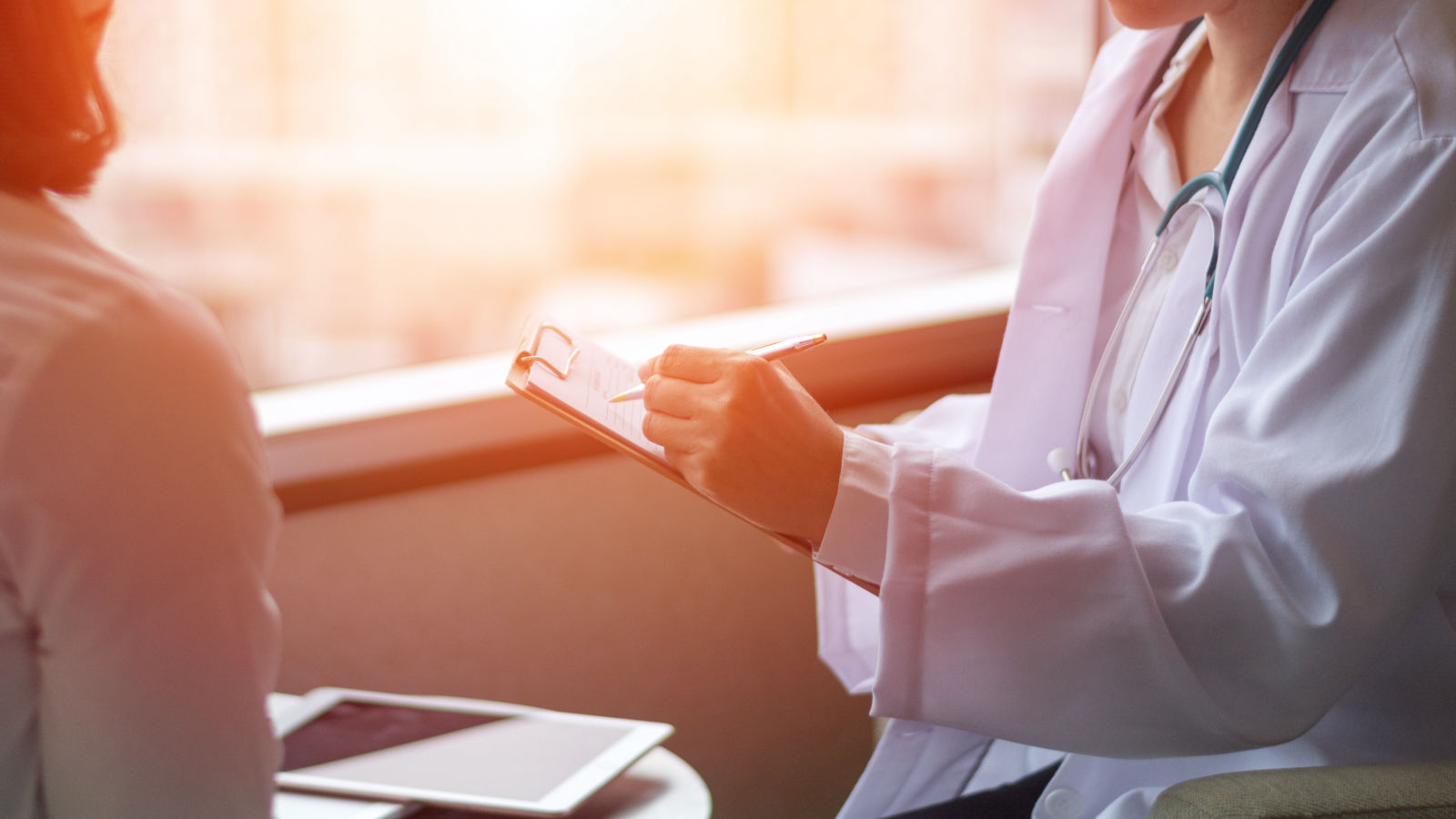 Generation Fertility specialist consulting with a patient while taking notes on a clipboard in a warmly lit medical office.